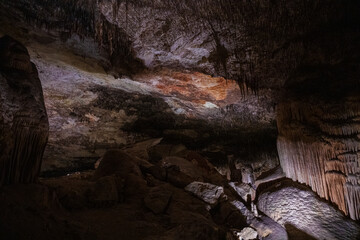 Large underground chamber filled with dense stalactites and rock formations, illuminated by soft artificial light inside a deep limestone cave