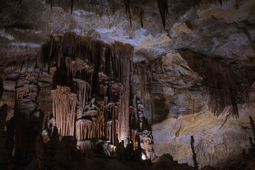 Large underground chamber filled with dense stalactites and rock formations, illuminated by soft artificial light inside a deep limestone cave