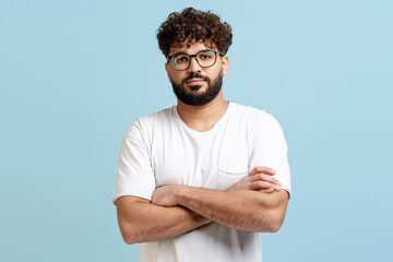 Confident young man with beard and curly hair posing with folded arms