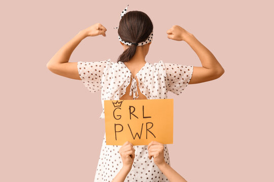 Female hands holding card with text GIRL POWER and pin-up woman showing her muscles on pink background, back view