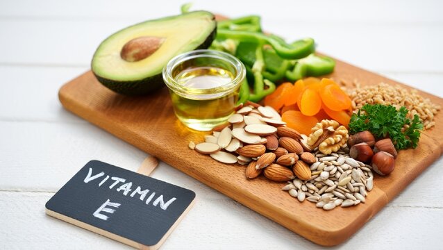 Assorted natural foods high in vitamin E arranged on a wooden board with chalkboard label. Includes avocado, nuts, seeds, oil, and vegetables.  AI generated.
