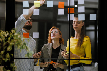 Group brainstorming session in a modern office with colorful sticky notes on glass wall during afternoon hours