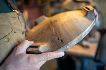 Carpenter checking material quality issues, holding wooden base with defects, cracks on items surface, small business owner producing unique handmade solid wood furniture in carpentry workshop.