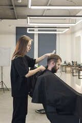 Professional woman barber wielding electric hair clipper making Fashionable haircut. Bearded Man client visit gentleman grooming beauty salon for hairstyle care. Modern Haircut style in barber shop