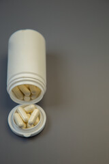 White pill bottle with capsules spilled out, showcasing the contents on a smooth gray surface, representing health, wellness, and pharmaceutical care in a minimalist setting