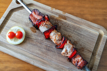 Grilled chicken and bacon skewers on a wooden cutting board, garnished with cherry tomatoes and lemon, perfect for outdoor barbecues and gatherings