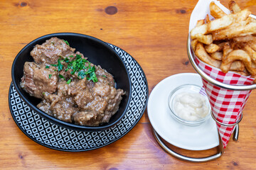 Hearty beef stew served in a decorative bowl alongside crispy fries and dipping sauce, showcasing a delicious culinary experience