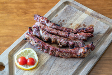 Grilled pork ribs served on a wooden cutting board with fresh lemon and cherry tomatoes, showcasing delicious barbecue cuisine and vibrant colors