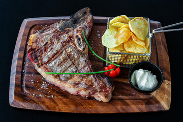 Grilled steak served on a wooden platter with crispy potato chips and fresh herbs, showcasing a delicious culinary presentation