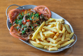 Delicious picadinha madeirense served with crispy fries and fresh tomato slices in a stylish metal platter, showcasing vibrant culinary presentation