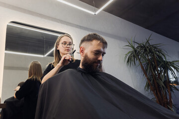 Woman Barber making customer Fashionable haircut in Modern style barbershop. Male hair cutting with scissors. Bearded Man client visit gentleman grooming beauty salon for hairstyle care