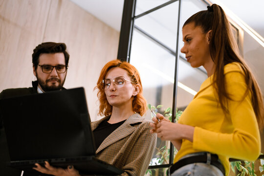 Team collaborates in modern workspace to discuss project details while reviewing laptop data during productive afternoon meeting