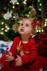 Little girl sitting near Christmas tree at the holiday