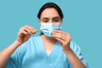Young female dentist in mask with dental mirror and tooth model on blue background