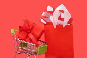 Small shopping cart with paper bag and gift boxes on red background. Valentine's Day celebration