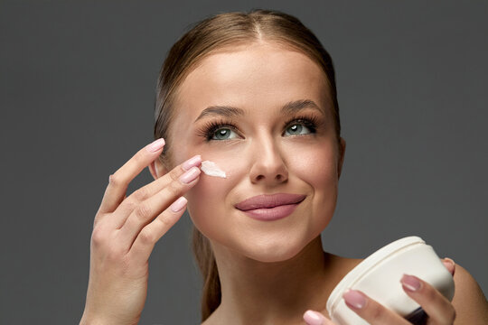 Woman applying cream on her face while smiling in a well-lit studio environment during a beauty session