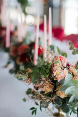 Coziness and style. Modern event design. Table setting at wedding reception. Floral compositions with beautiful flowers and greenery, candles, laying and plates on decorated table.