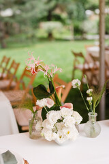 Coziness and style. Modern event design. Table setting at wedding reception. Floral compositions with beautiful flowers and greenery, candles, laying and plates on decorated table.