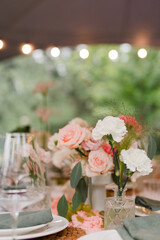 Coziness and style. Modern event design. Table setting at wedding reception. Floral compositions with beautiful flowers and greenery, candles, laying and plates on decorated table.