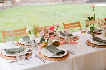Coziness and style. Modern event design. Table setting at wedding reception. Floral compositions with beautiful flowers and greenery, candles, laying and plates on decorated table.