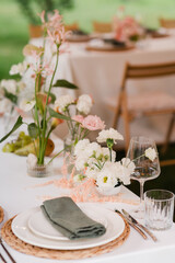 Coziness and style. Modern event design. Table setting at wedding reception. Floral compositions with beautiful flowers and greenery, candles, laying and plates on decorated table.