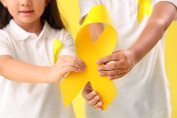 Cute little children with yellow ribbons on color background. Childhood cancer awareness concept