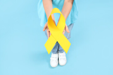 Little girl with yellow ribbon on blue background. Childhood cancer awareness concept