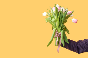 Male hand with bouquet of beautiful tulips on yellow background. International Women's Day
