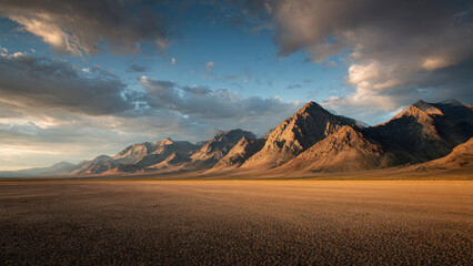 Dramatic desert landscape at golden hour, featuring a vast dry lakebed (playa) stretching towards rugged mountains under a cloudy sky.