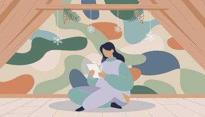 Relaxing winter lifestyle Woman sits in cozy attic using a glowing tablet decorated for the holidays