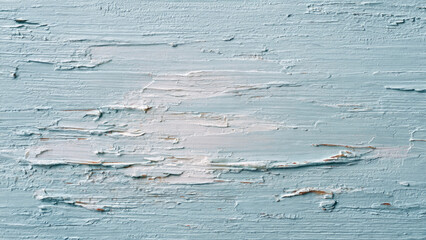 Close-up of weathered pale blue paint peeling and flaking from a surface, revealing lighter layers and texture underneath, creating an aged, distressed background.