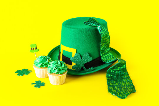 Tasty cupcakes with leprechaun hat, tie and decor for St. Patrick's Day on yellow background
