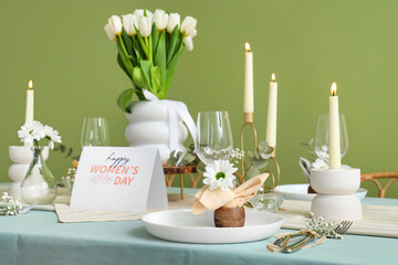 Beautiful table setting with burning candles and tulip flowers for International Women's Day celebration near green wall