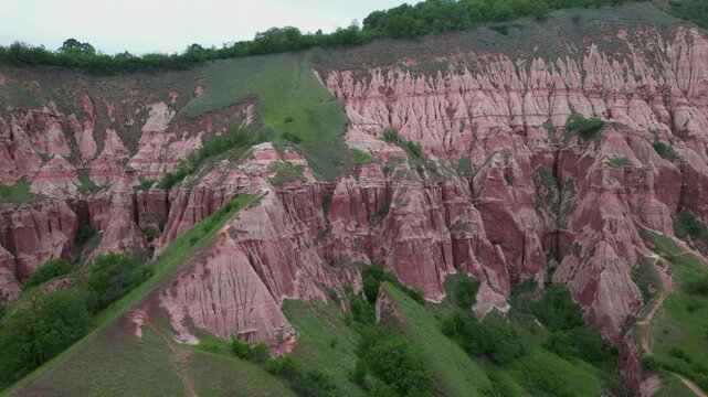 Reddish rock formations and green slopes of the Rapa Rosie natural monument in Transylvania