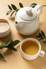 Teapot with cups of tea and leaves on beige grunge background