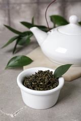 Board with teapot, bowl of dry tea and leaves on grunge table against grey tile background