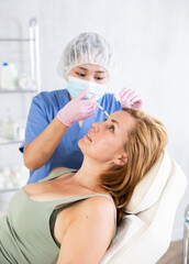 Fototapeta premium Young qualified doctor giving injections in face of patient in clinic