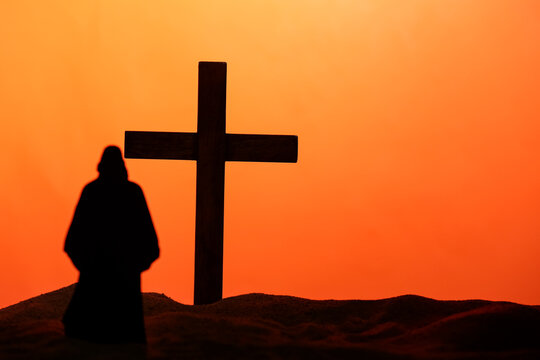 Jesus with wooden cross on sand against orange background. Good Friday concept