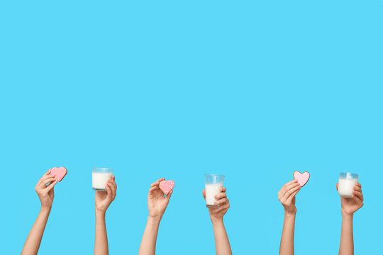 Women with heart-shaped cookies and glasses of milk on blue background. Valentine's Day celebration