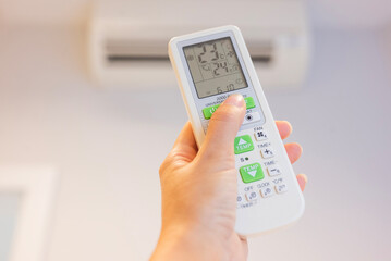 A girl controls the air conditioner by adjusting the temperature with the remote control. The air conditioner is in her hand.