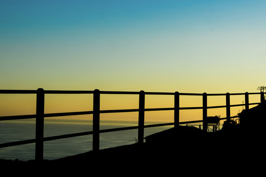 Silhouette of mountain road railing above sea at sunset, dramatic coastal travel landscape with vivid sky