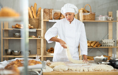 Female cook is working with dough, weighing piece of dough on scale. She prepares blanks for baking buns and croissants, determines weight of dough pieces