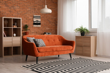 Stylish interior of loft style living room with orange sofa, chest of drawers and shelving unit