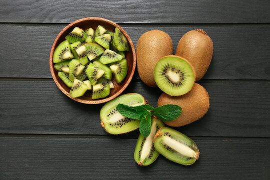 Bowl with pieces of fresh kiwi and mint on black wooden background - Powered by Adobe