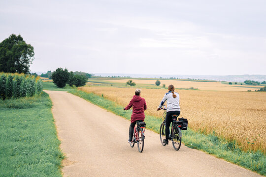 Two unrecognizable women cycling together along a countryside path surrounded by fields. Concept of health, fitness, outdoor sports and daily physical activity in a natural environment.