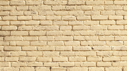 Obraz premium A weathered brick wall painted in a warm, creamy beige, revealing texture and subtle signs of age and sunlight.