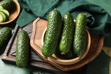 Wooden bowl with fresh cucumbers on green background