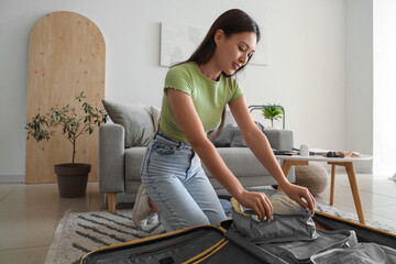 Female Asian traveler with organizers packing suitcase at home