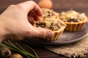 Tartlets with meat and cheese with hand on brown wooden, linen textile. side view, close up, selective focus