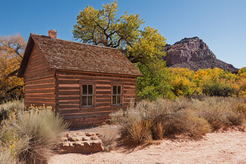 The one-room log cabin historic Fruita schoolhouse in Capitol Reef National Park in the Fall, trees...